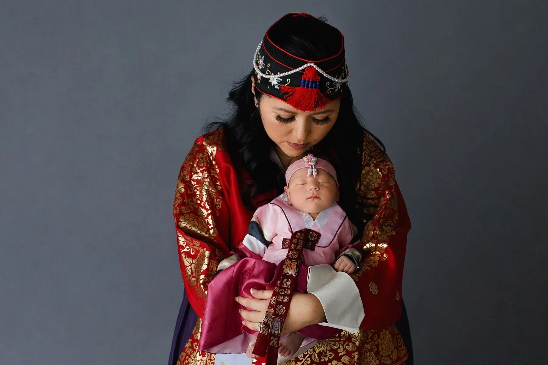 High end fine art studio Newborn baby girl boy neutral Image hanbok Korean asian heritage culture colorful sleeping bundle photographed by Cynthia Hamilton Photography in Austin, Texas Mother holding baby in traditional hanbok.